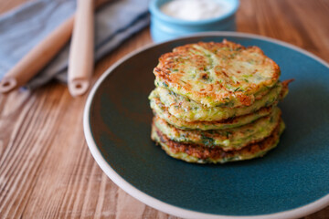 Vegetarian food. Zucchini fritters, thin pancakes and sauce on white plate over wooden table. Squash pancakes