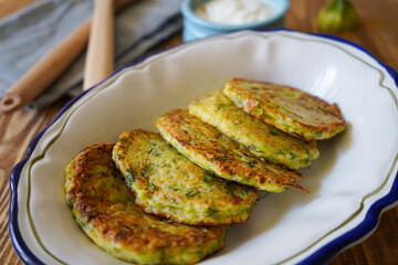 Vegetarian food. Zucchini fritters, thin pancakes and sauce on white plate over wooden table. Squash pancakes