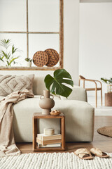 Stylish composition of living room with design beige sofa, wooden stool, tropical leaf in vase,...