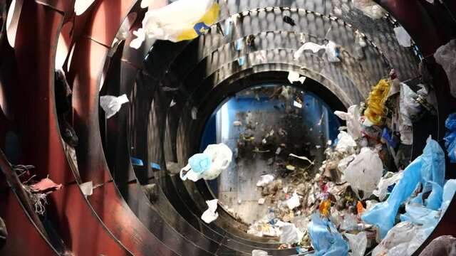 Plastic bags are spun in the drum of a special sorting machine for the separation of mixed waste at the enterprise for the processing and disposal of household garbage in slow motion.