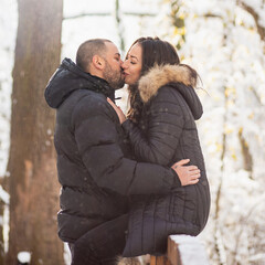 Fototapeta premium Man and woman in love hugging and kissing on a bridge. Snowy winter background.