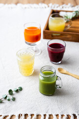 Verschiedene gesunde Säfte in Gläsern und ein Holz Serviertablett auf einem beigen Leinen Tischtuch.