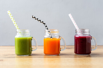 Variation von Säften auf einem Holztisch in einer Reihe mit Strohhalm. Gesundes Frühstück, grauer Hintergrund.