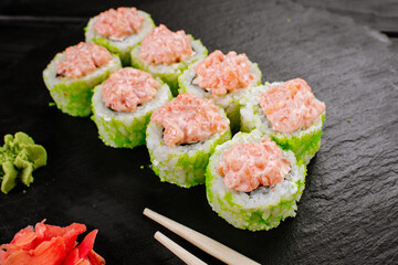 Green sushi rolls with salmon sauce on black background