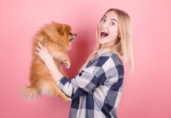 A cute young woman is holding her Pomeranian puppy. Love between owner and dog. Isolated over pink background. Studio portrait.