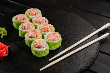 Green sushi rolls with salmon sauce on black background