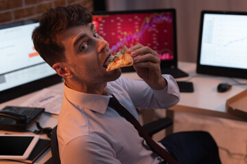 Businessman looking at camera while eating pizza in office at evening