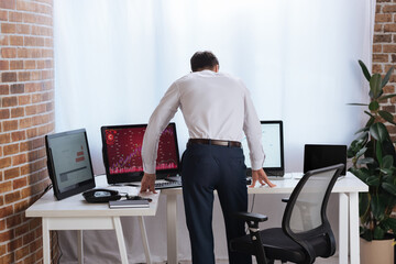 Back view of forex businessman standing near computers with charts in office