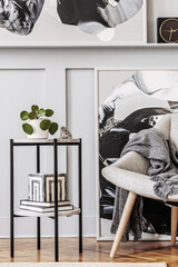 Stylish scandinavian home interior of living room with design gray armchair, modern stool, black coffee table, modern paintings, decoration, plant and elegant personal accessories in home decor.