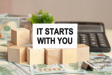 Paper card with text IT STARTS WITH YOU. Calculator, flowers and brown background