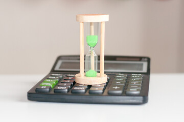 calculator and hourglass close-up stand on a white wooden table, business concept