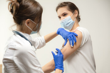 Treatment. Close up doctor or nurse giving vaccine to patient using the syringe injected. Works in face mask. Protection against coronavirus, COVID-19 pandemic and pneumonia. Healthcare, medicine.