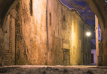 Beautiful narrow street of Vilnius Old Town, evening or night view with old buildings and street lamp in winter with snow