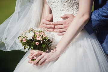 the groom embraces the bride. hands of the bride with a bouquet of pink and white flowers. tenderness, wedding.