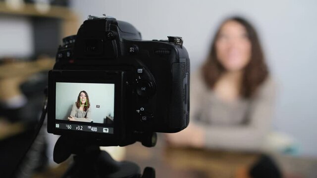 Young smiling woman sitting at the desk talking to the camera while taking a shot. Vlog and freelancer concept.