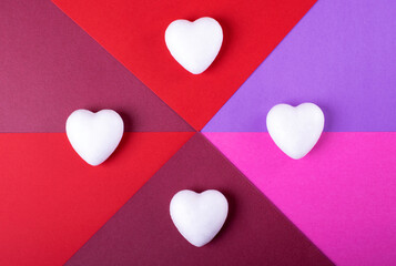 Geometric backdrop for Valentine's Day. White hearts against the pink, red and purple background. Flat lay