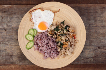 Thai fusion stair fried chicken with Thai basil and cashew nut with health brown rice fried egg sauce cucumber on woody plate over rustic wood background