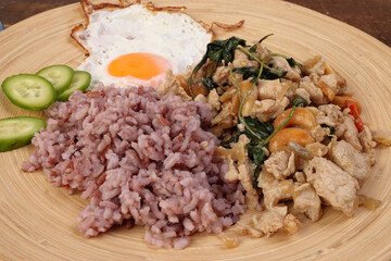 Thai fusion stair fried chicken with Thai basil and cashew nut with health brown rice fried egg sauce cucumber on woody plate over rustic wood background