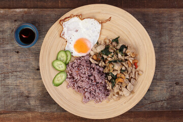 Thai fusion stair fried chicken with Thai basil and cashew nut with health brown rice fried egg sauce cucumber on woody plate over rustic wood background