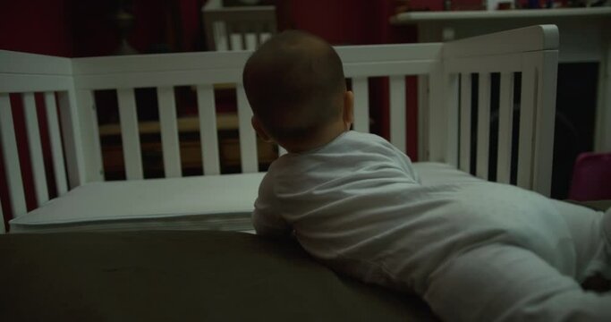 A little baby is crawling on a bed by his bedside cot