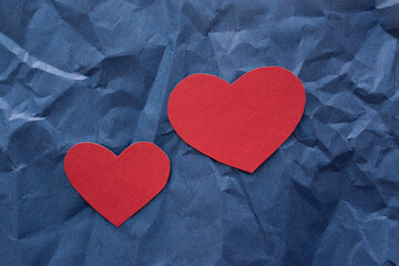 Two hearts made of red cardboard, one small, the other large, lie on a blue background of crumpled paper