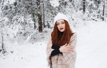 Fototapeta na wymiar A young girl with long bright red hair on a winter background.A red-haired woman in a white cap.