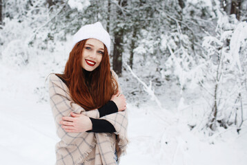 Fototapeta na wymiar A young girl with long bright red hair on a winter background.A red-haired woman in a white cap.