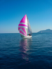 sail boat yacht regatta race with large colorful pink and grey spinnaker blue sea and sky and...