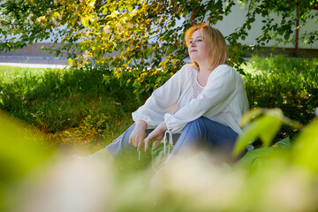 Outdoor portrait of a beautiful blonde middle-aged woman near blossom apple trees with white flowers.