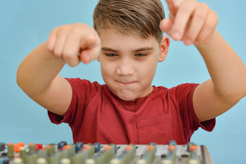 The boy controls the equalizer on the mixing console in the music studio.