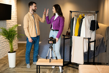 Young bloggers finished filming their vlog indoor about selling clothes and giving five each other for good job.