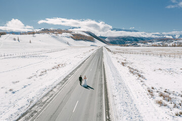 Bride and groom in a dress on a snowy road among the mountains in autumn in Altai