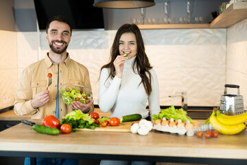 Young and beautiful vegetarian couple are smiling in the kitchen while cooking. Also they look happy and healthy because of using only nutrition and fresh food.