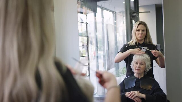 Reflection In Mirror Of Senior Woman Having Hair Cut By Female Stylist In Hairdressing Salon