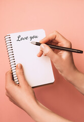 Woman's hand holding pen and open spiral notebook with the inscription I love you on light background. Planning concept