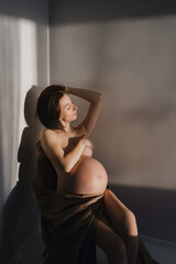 Naklejka premium Young pregnant girl without clothes in the rays of the sun in the bedroom by the wall