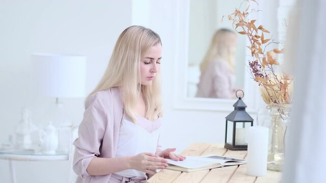 young beautiful woman reads a book at the table in the living room. soft focus. selective focus. Selective focus. Slow motion video. stock footage