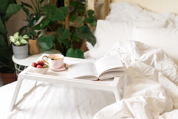  Breakfast in bed. Heart shaped white plate with fresh strawberries, cup of coffee, book and plants flowers. Still life composition. Mother, Valentine day concept.