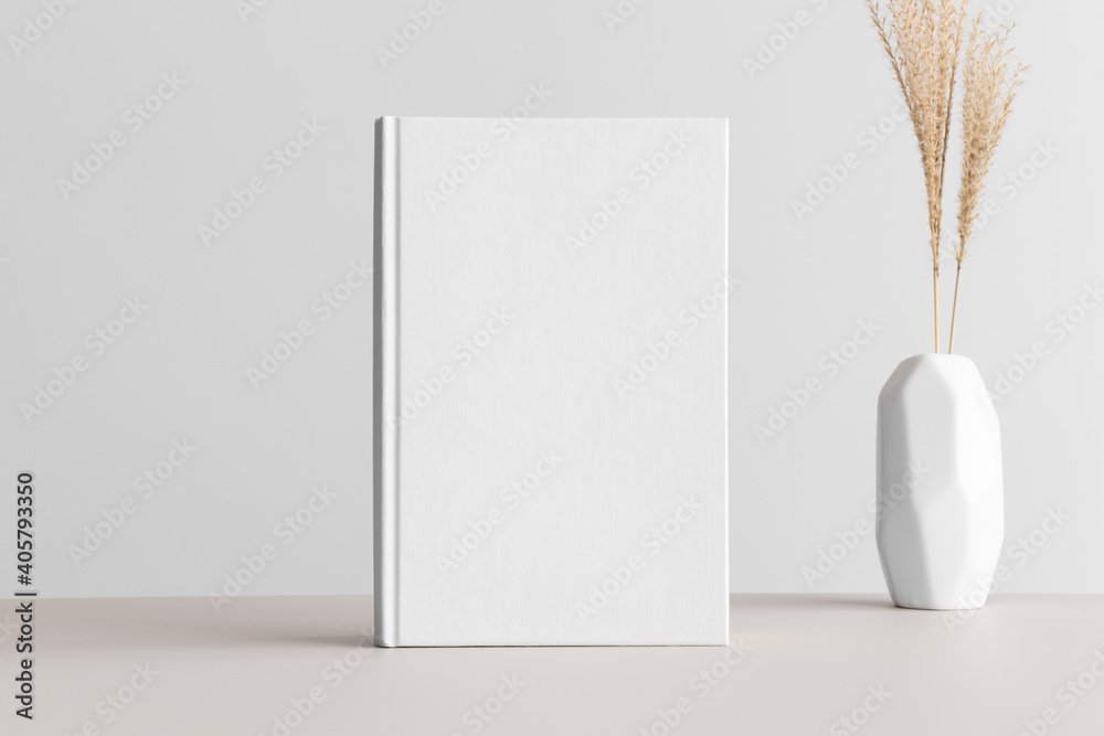 Wall mural White book mockup with a dried grass in a vase on the beige table.