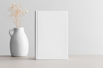 White book mockup with gypsophila in a vase on the beige table.