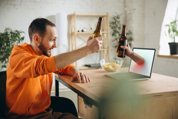 Friend. Young man drinking beer during meeting friends on virtual video call. Distance online...