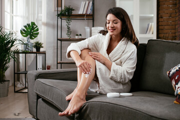 Beautiful woman in bathrobe applying body cream. Smiling woman enjoying after bathing at home..