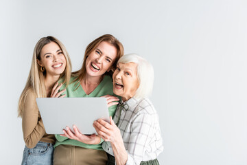 three generation of joyful women looking at camera near laptop isolated on white