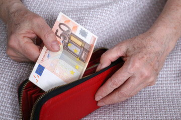 Elderly woman takes out a euro note from her wallet. Concept of pension payments, savings at retirement, pensioner with money