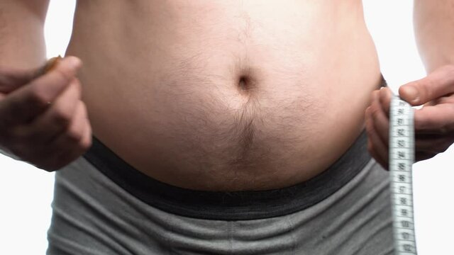 A fat man measures his waist, a big beer belly, a healthy lifestyle picks up fat folds