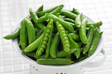 freshly picked green pea pods in enamel colander