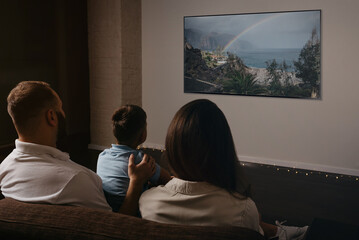 A photo from behind of a father, a son, and a young mother which are watching a movie on a...