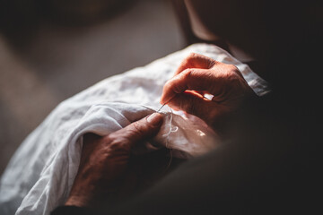 Female holds a needle in her hands and embroiders a pattern with white threads on a white cloth