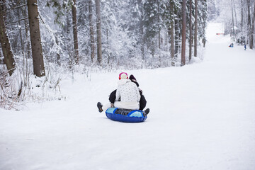 Fototapeta na wymiar Mother and child sliding on snow tubing down the hill. Winter entertainment.