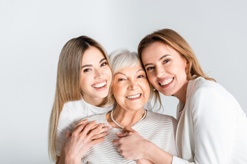 three generation of positive women smiling while looking at camera and hugging isolated on grey - obrazy, fototapety, plakaty